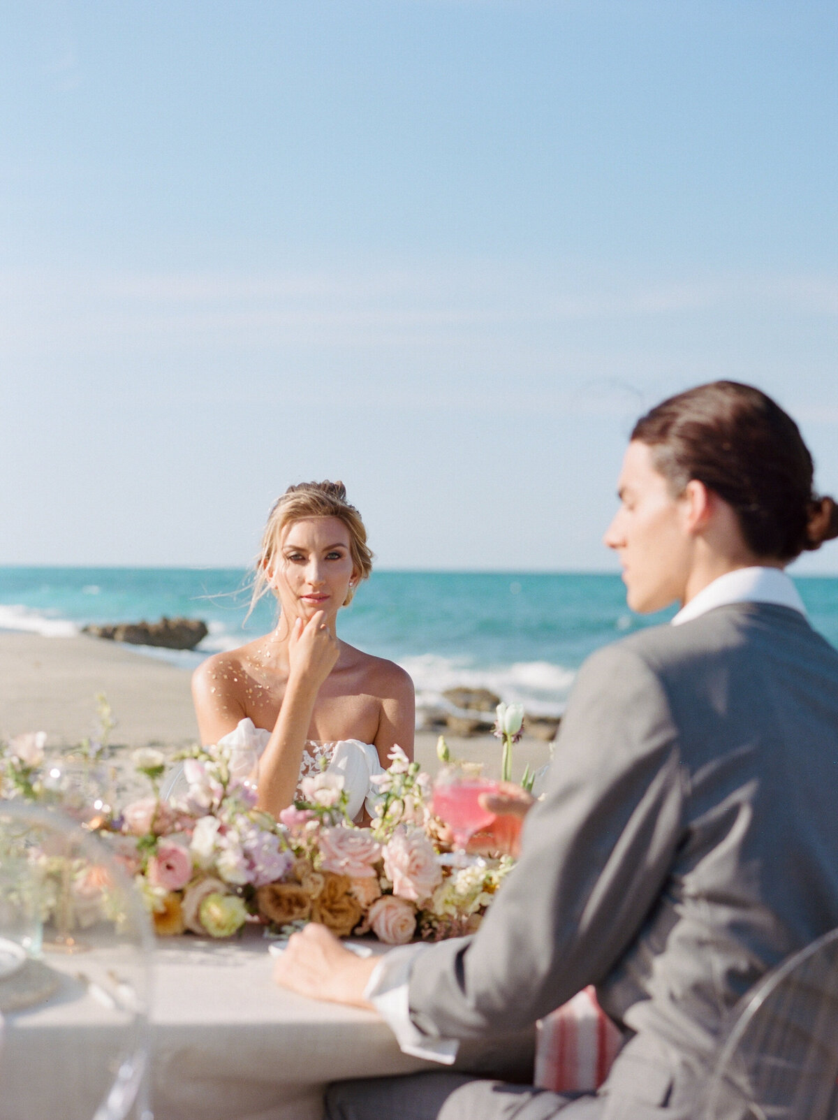 Couple sits down at fancy table at beach.