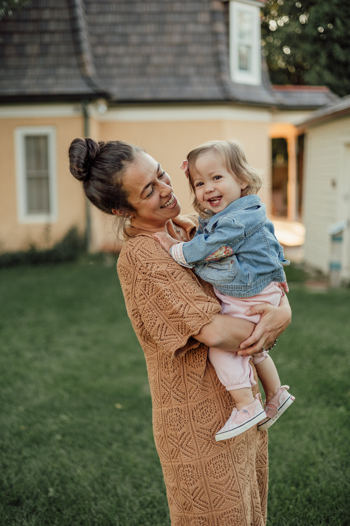 mom holding baby girl in jean jacket laughing during lifestyle family session with alexis adkins photography in firestone colorado