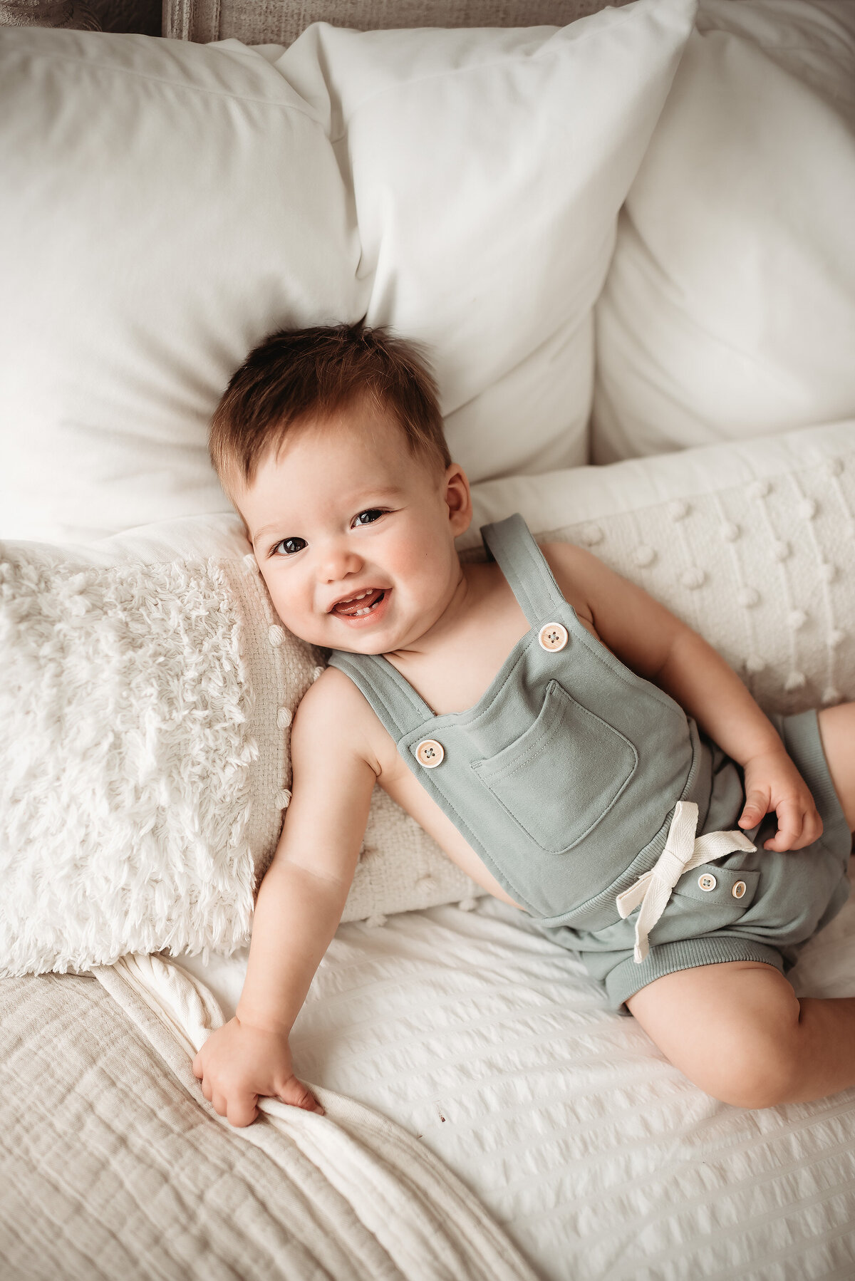 one year old boy in sage green romper lying on milestone photographer's couch