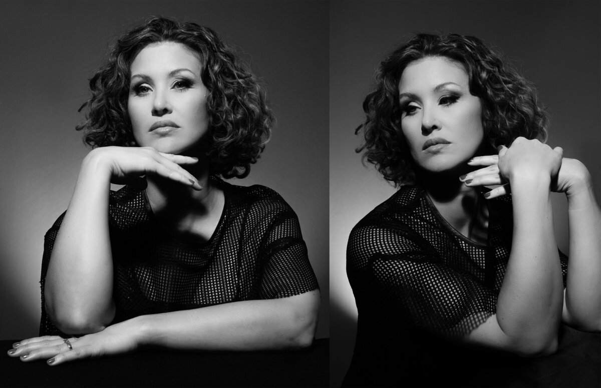 A woman with natural curly and wavy hair looks away from camera as she poses for a black and white portrait in old Hollywood glamour style lighting