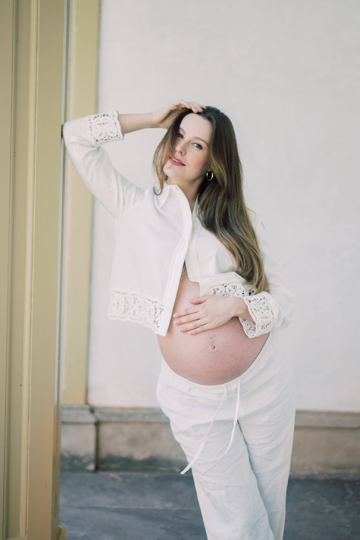 Softly lit color image of a pregnant woman embracing her belly, styled in all-white Zara pieces
