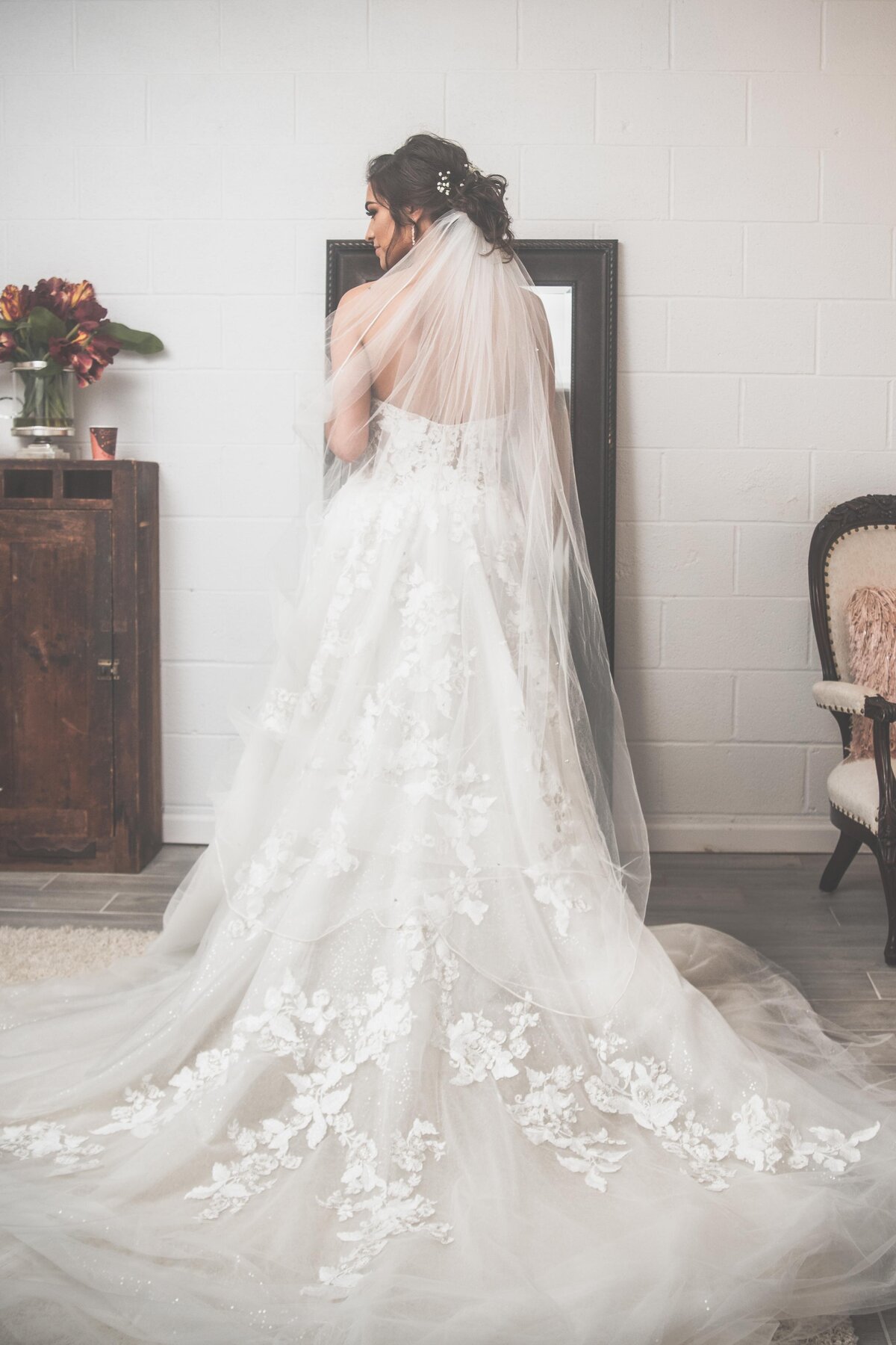 a bride stands with her back to the camera, her lace veil falling around her