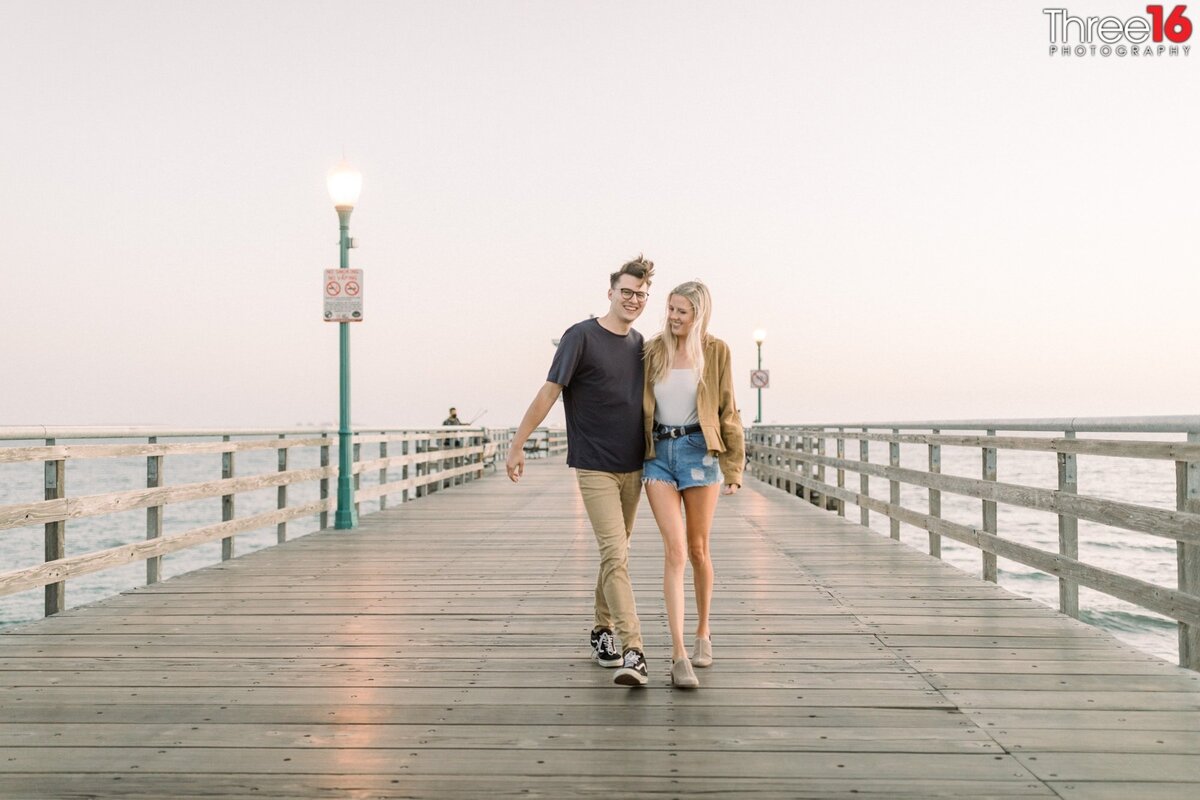Engaged couple walk together along the Seal Beach Pier