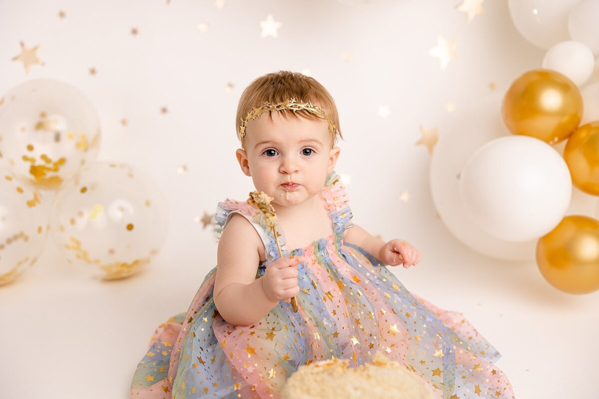 baby girl eating cake for cake smash pictures in rainbow dress