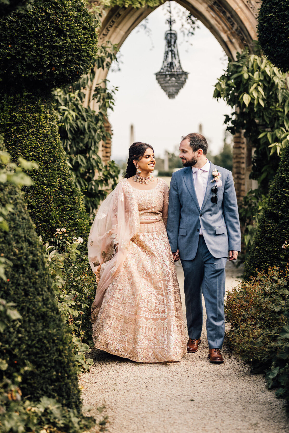 Bride of Indian Heritage walking through lush gardens with Groom