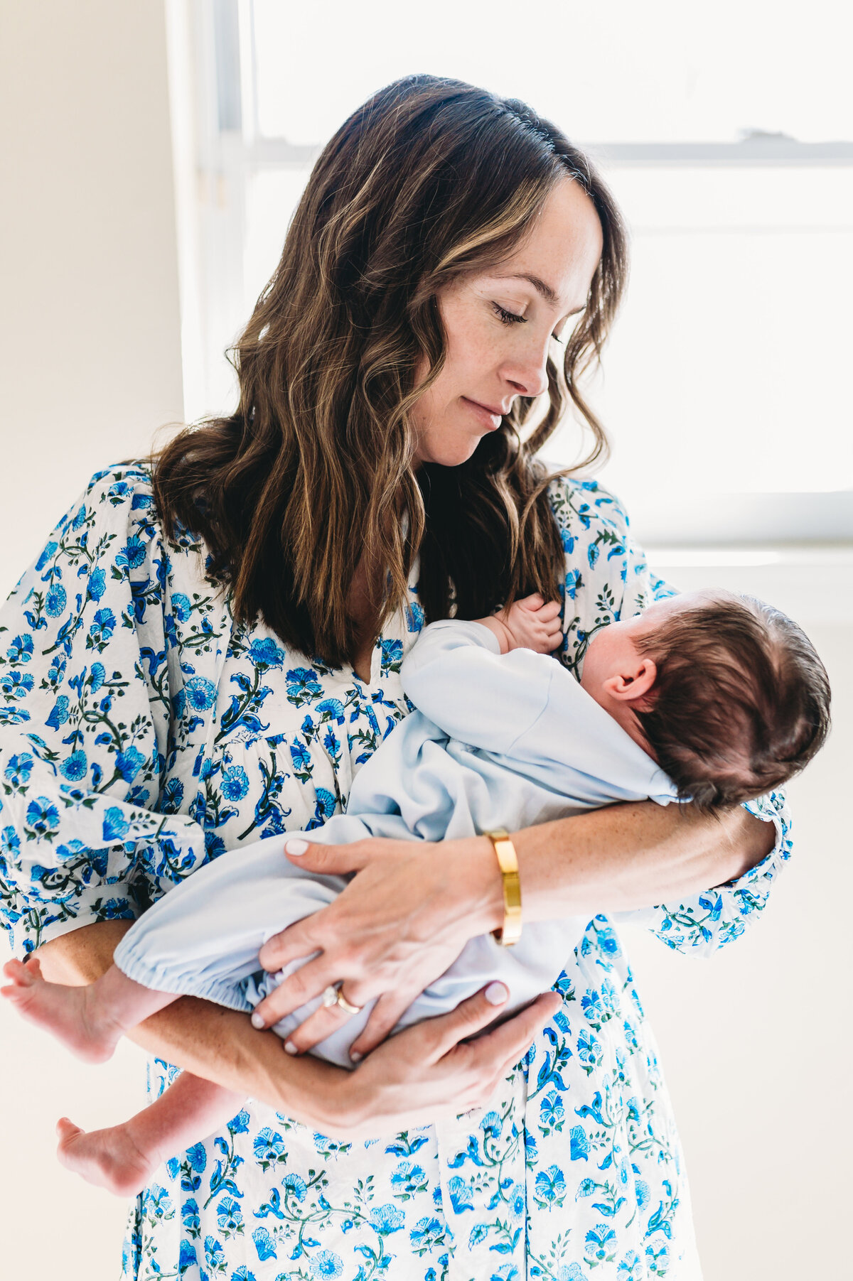 mother in blue floral dress holds new baby boy at home