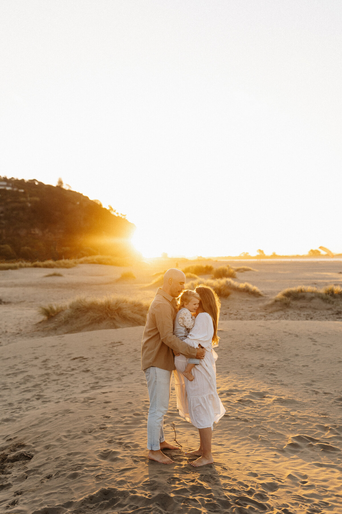 A mother and father holding their little baby during a sun set family photoshoot with lucy jane photography in christchurch