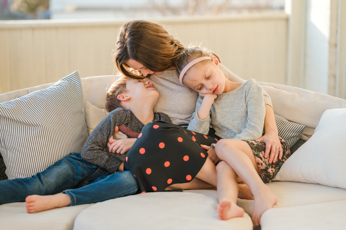 Mom snuggles her kids on a daybed during golden hour family pictures.