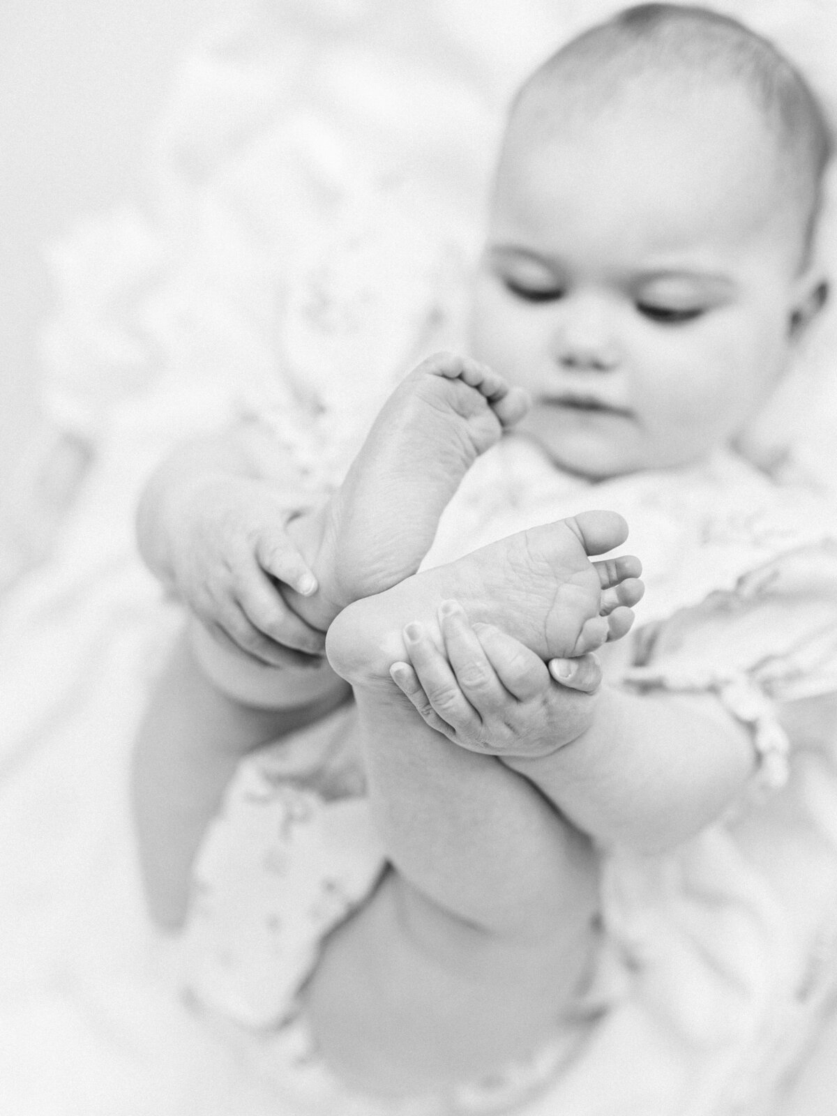 Black and white photo of a baby holding her feet with her hands 