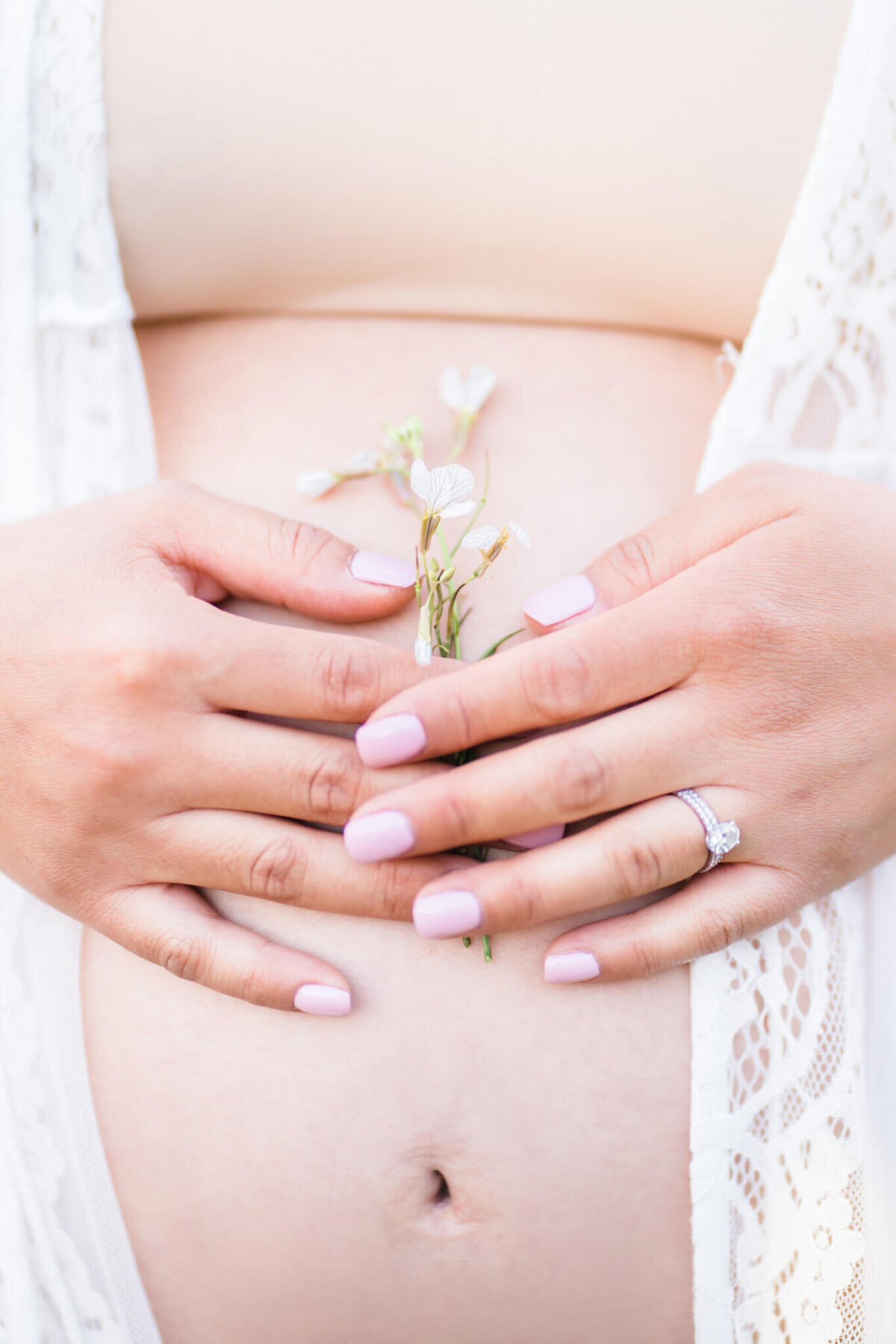 Bare exposed pregnant belly with lace coverup with hand holding flowers