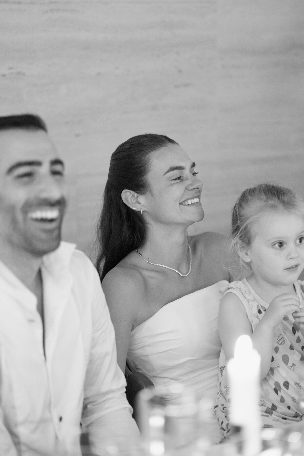 Bride smiling with groom and flower girl at wedding dinner table

