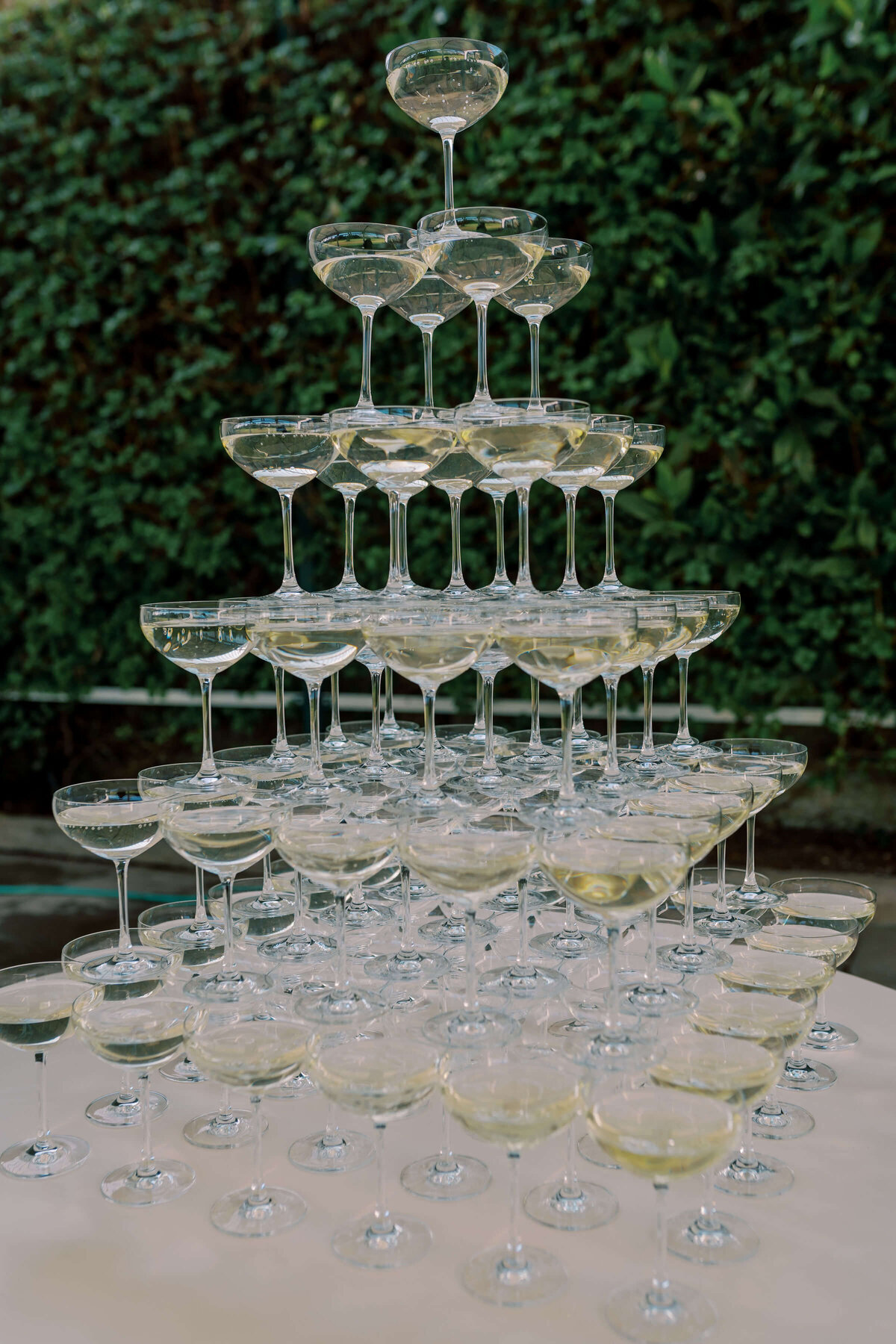 six tier champagne tower displayed on a white table in front of a foliage wall backdrop at luxury wedding venue avington park for a westacott wedding