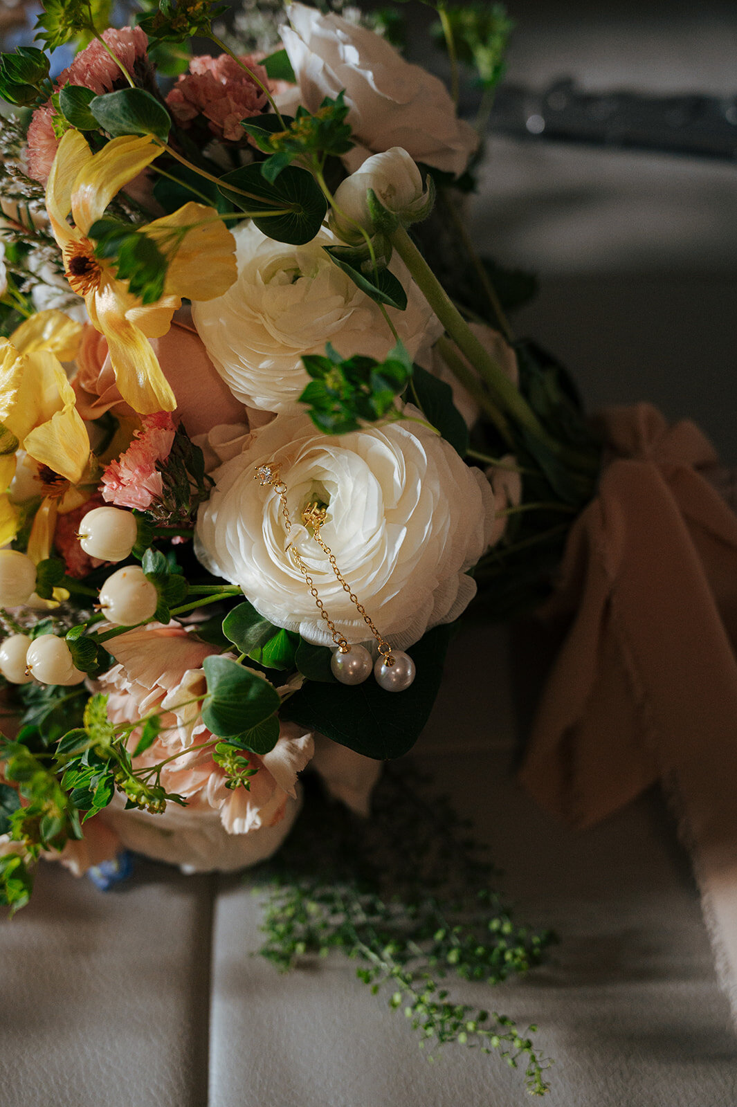 A close up of a flower bouquet with pearl earrings dangling from it.