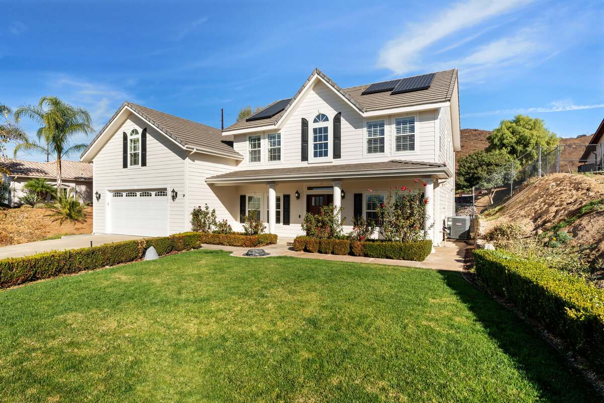 Front of a large white two story home in Ramona, California. Home has a porch overhang and green grass.