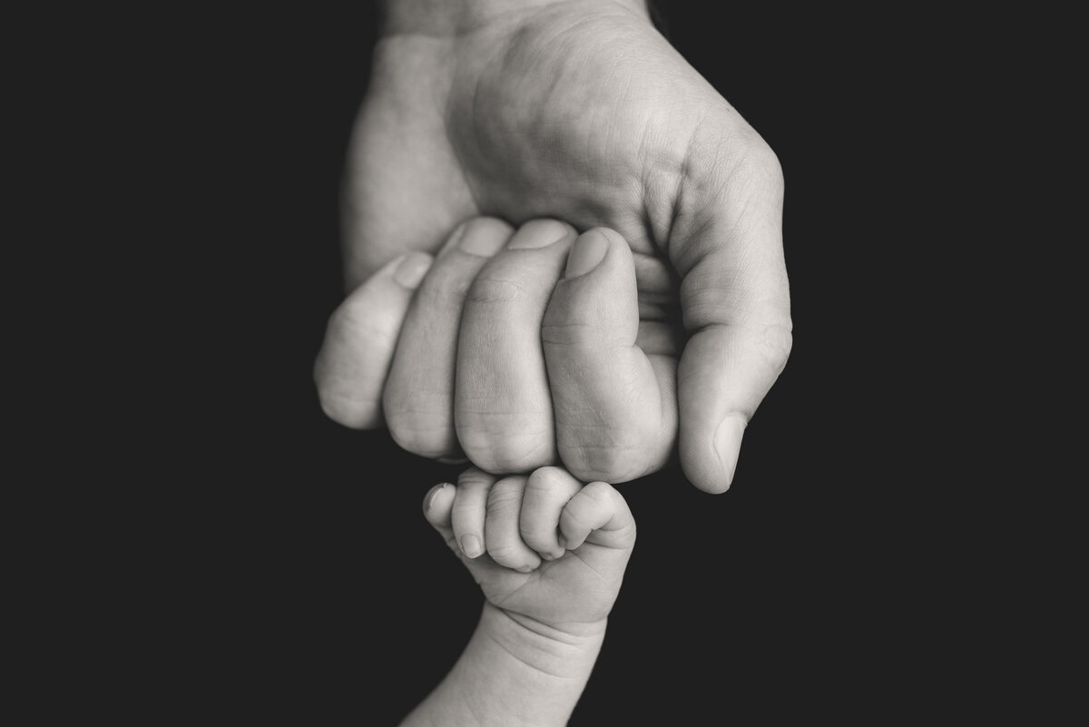 Black and White image of baby's fist and Dad's fist touching