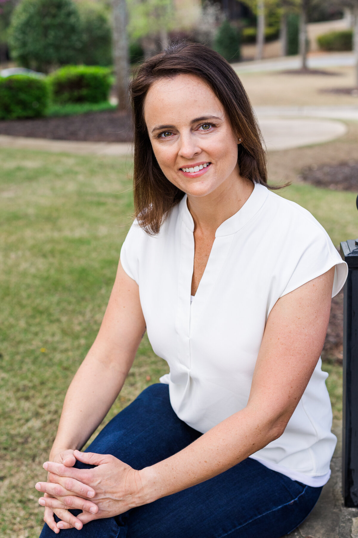 woman in casual jeans and white top outfit sitting hands on knees in a park