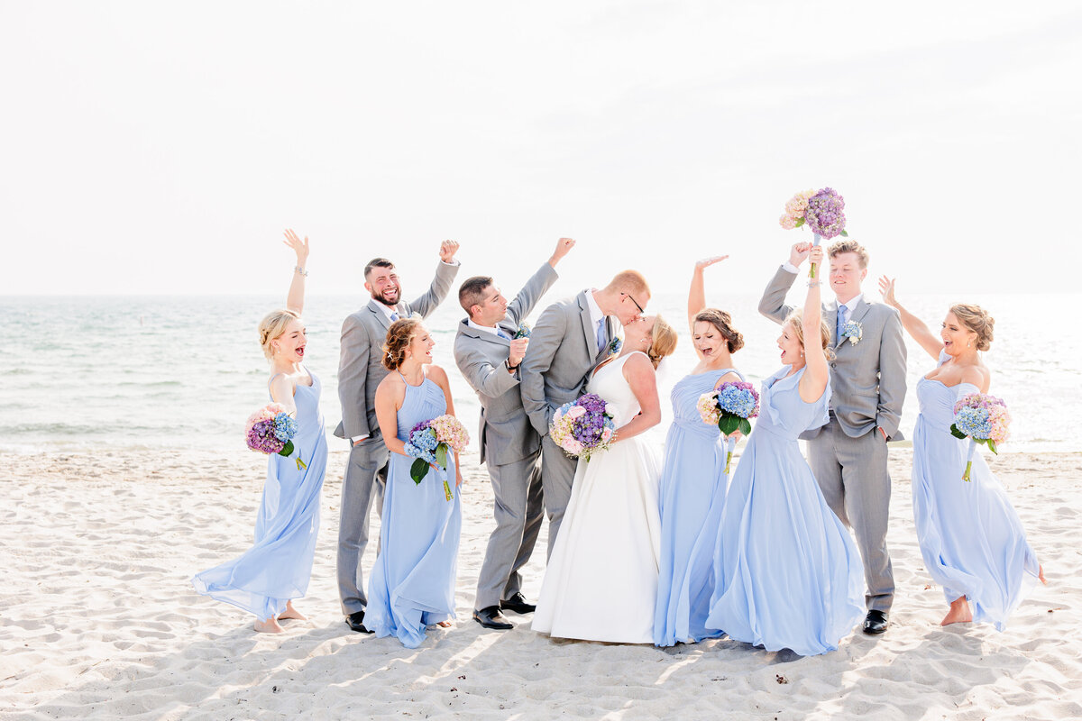 Wedding party cheering while the bride and groom kiss representing joyful Cape Cod wedding pictures