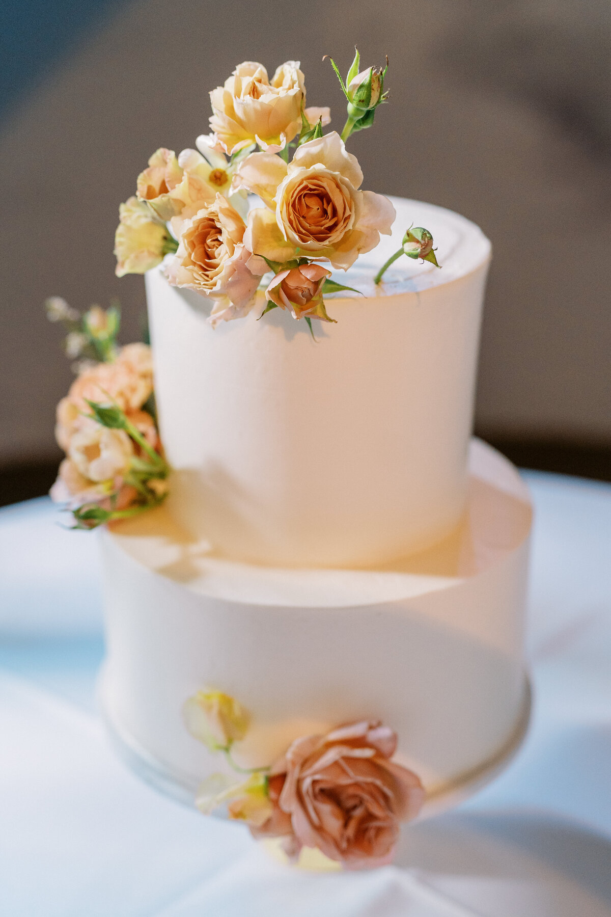 Two-tier wedding cake decorated with peach and ivory roses and delicate floral accents.