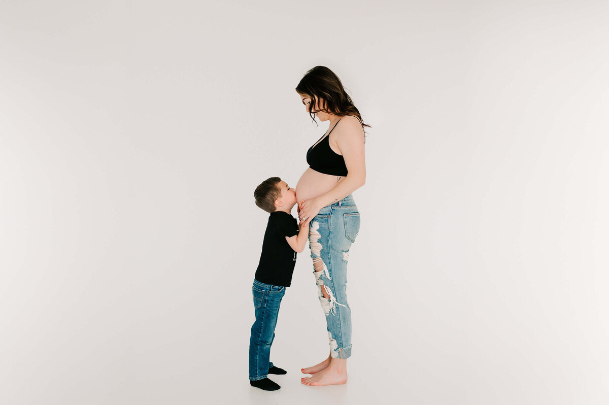 toddler son kissing pregnant mom belly during studio maternity photography in Springfield MO