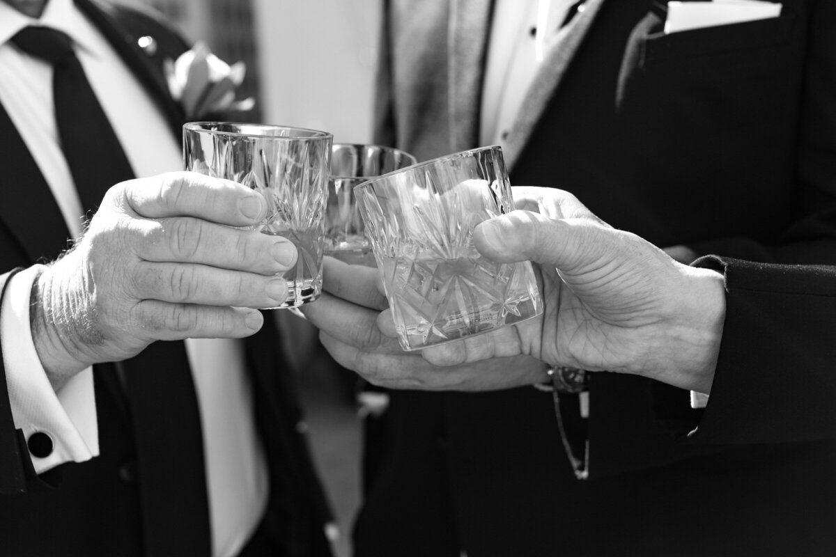 close up of whiskey glasses raised by the groom and groomsmen at The Adolphus in Dallas, capturing a celebratory and stylish wedding moment.