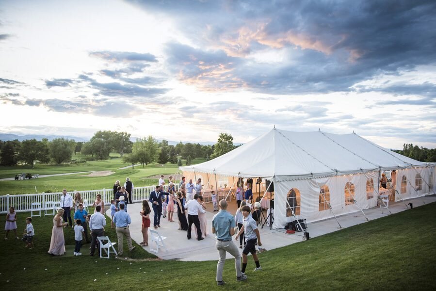 A wide angle shot of an outdoor tented wedding reception with sunset clouds in the background.
