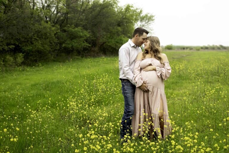 A tender maternity photo of the husband and wife standing together in the park, with the husband gently resting his hands on his wife’s baby bump, captured in a loving moment by Chunky Monkey Photography.