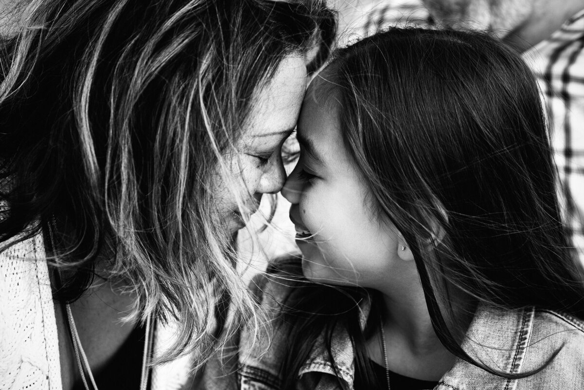 Black and white image of Latin mom and daughter nose to nose, hair blowing, in Jacksonville, FL.