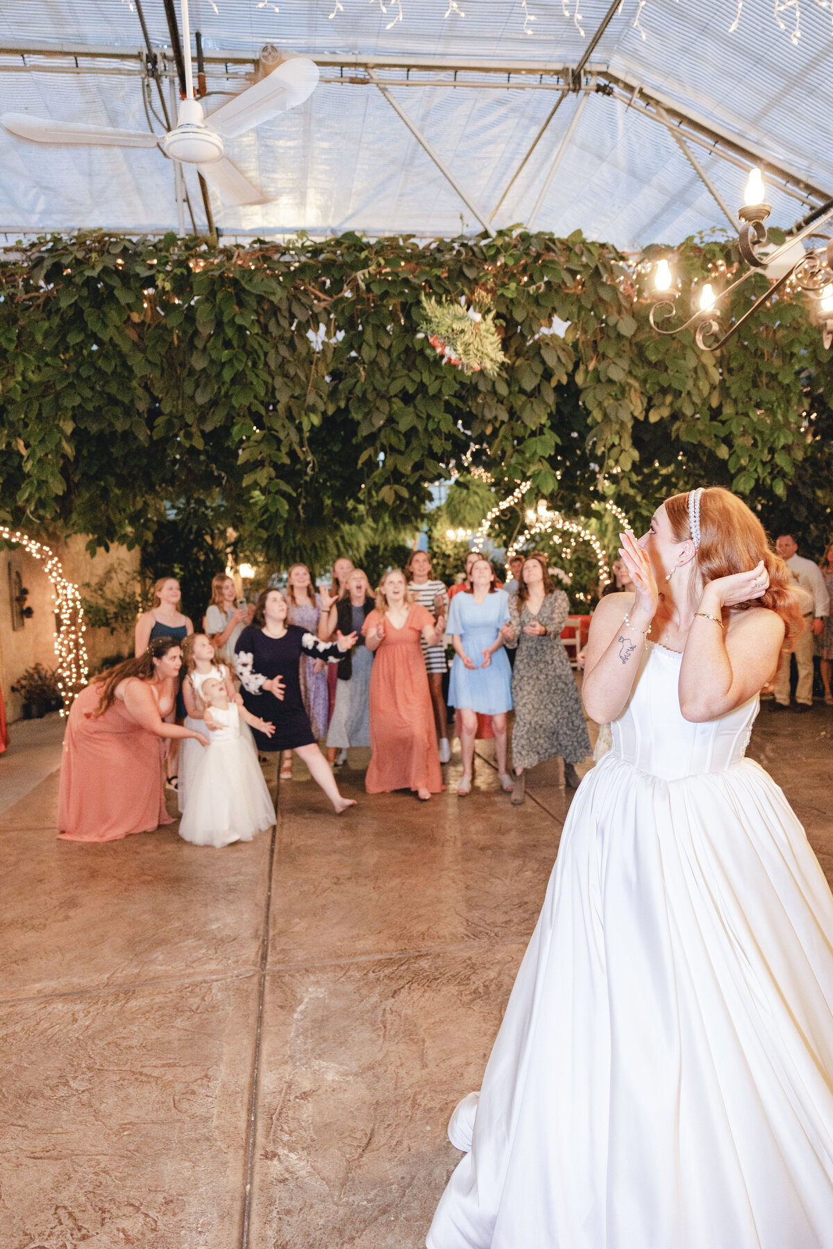 The bouquet soars through the air as a group of excited guests anticipate catching it, set against the beautifully decorated venue.