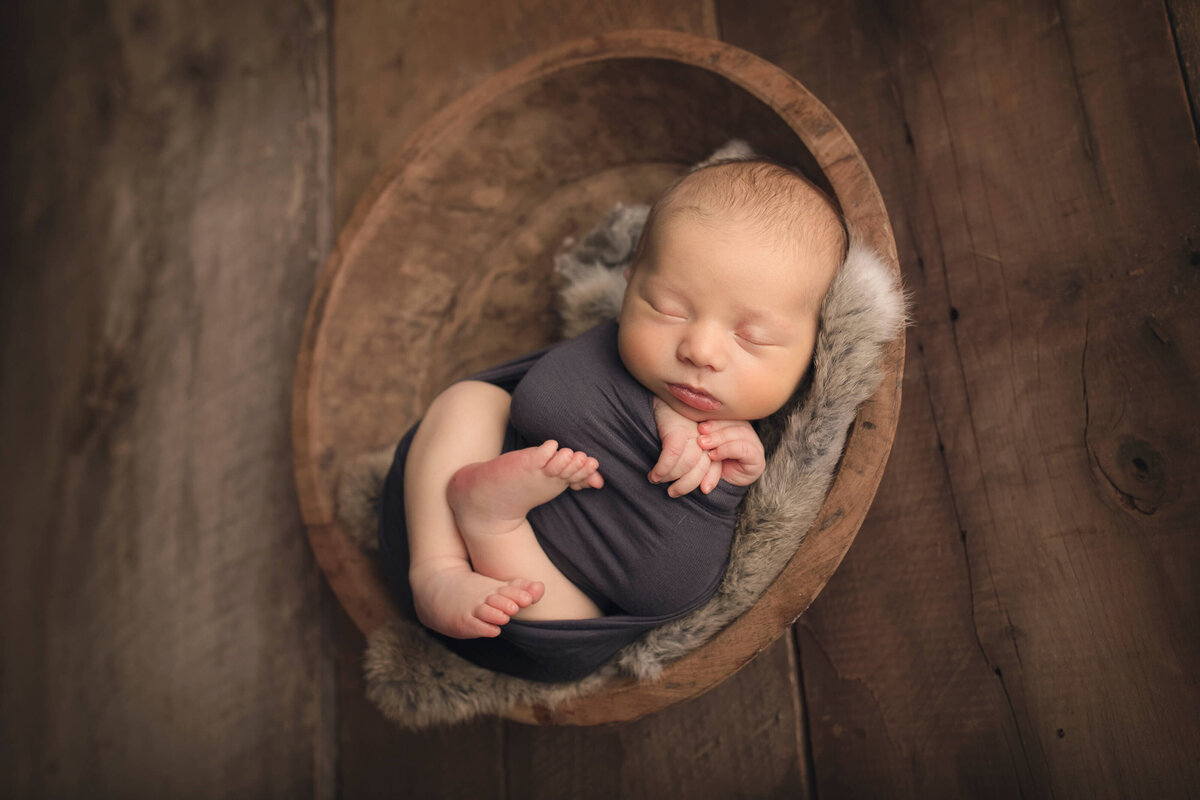 newborn baby boy posed in wooden bowl