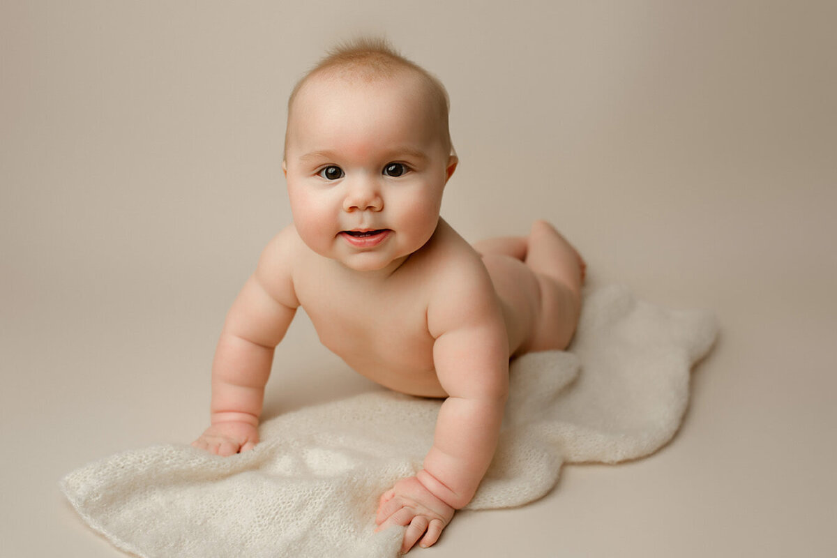 A baby boy does tummy time on a white backdrop