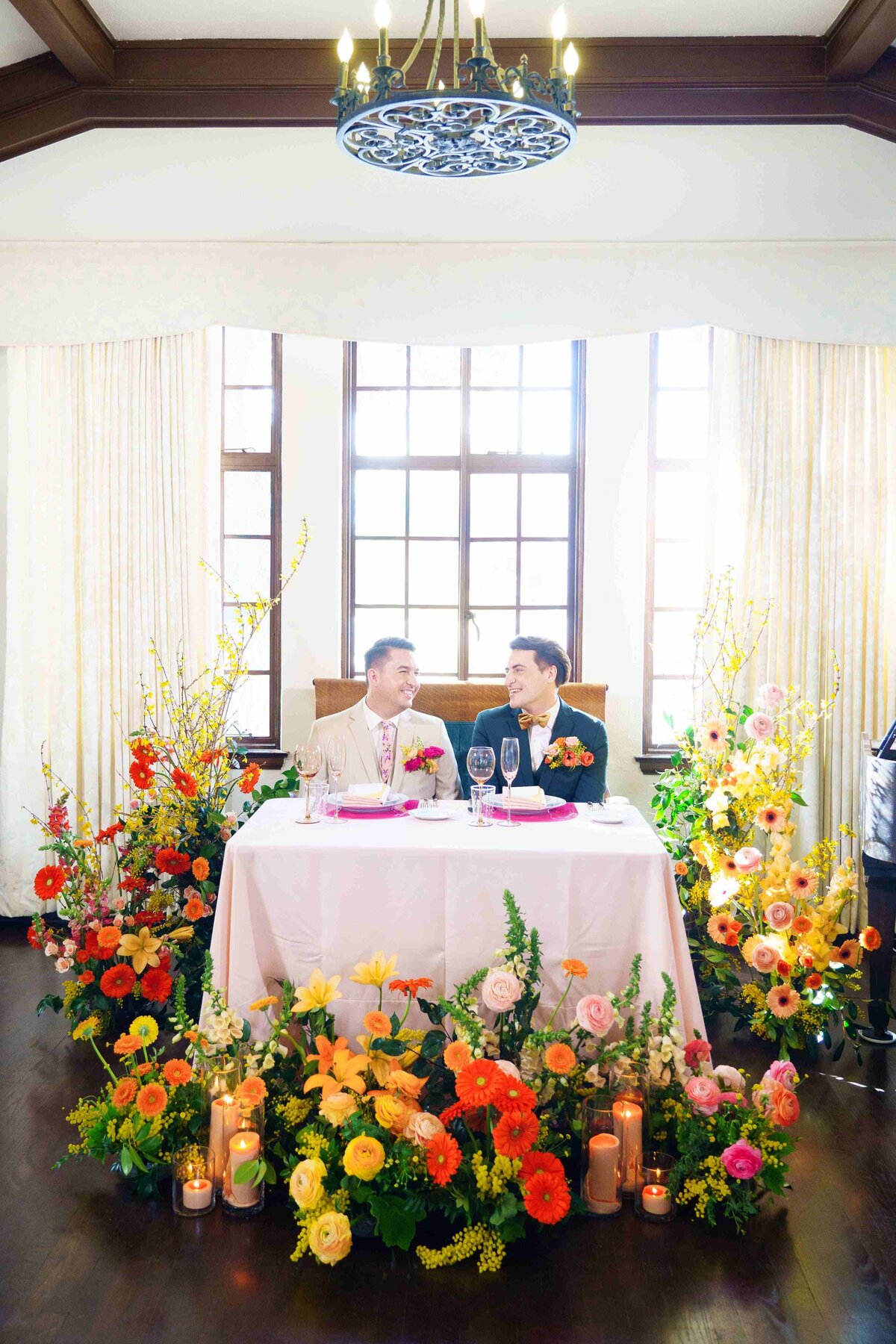 Two grooms at their sweetheart table surrounded by colorful flowers at The Ebell Santa Ana