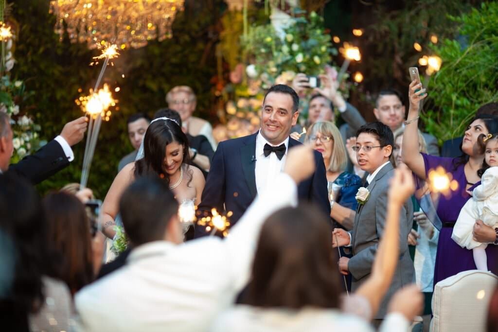 A bride and groom walking between their guests holding sparklers