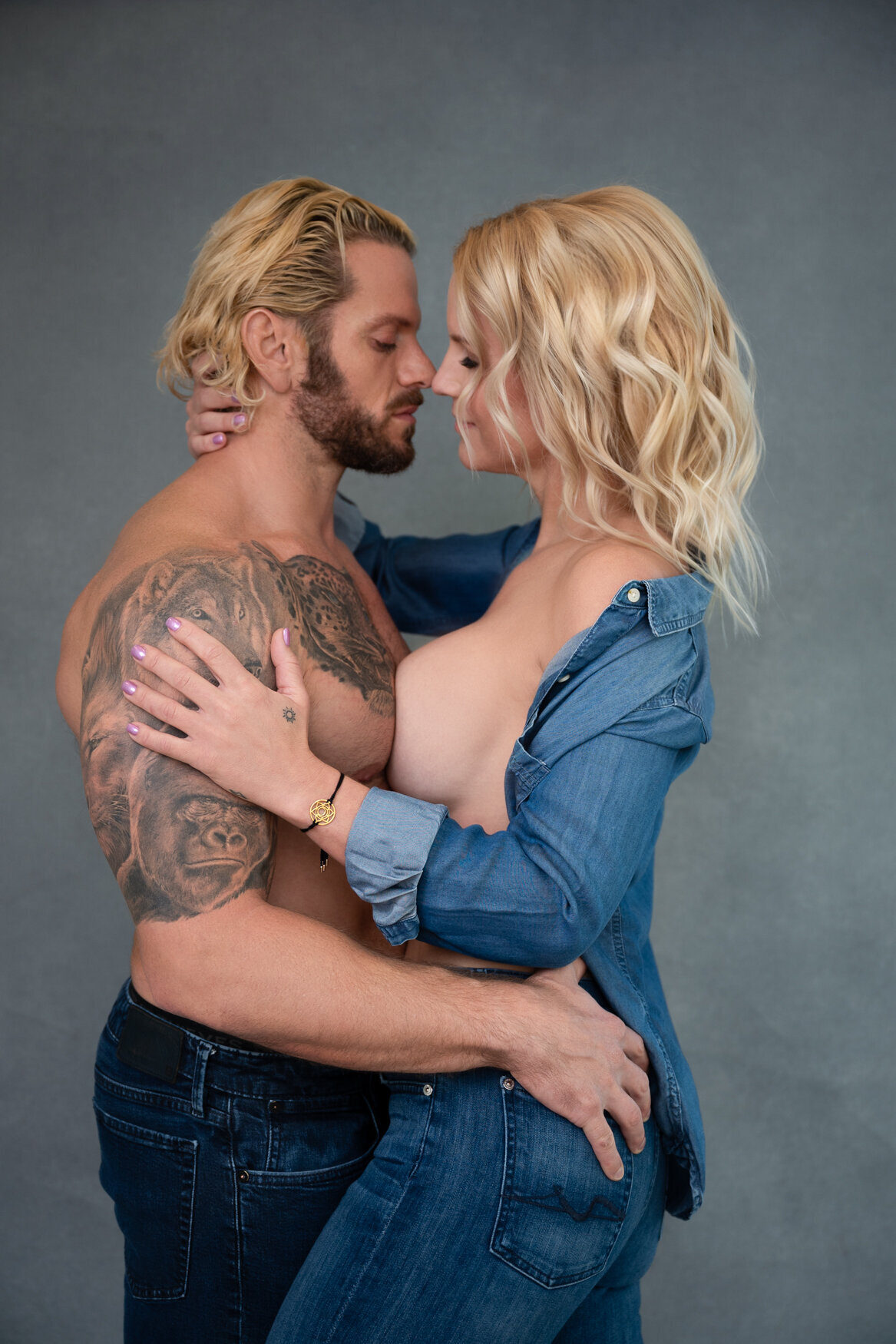 Intimate couple's portrait with a woman in a partially unbuttoned denim shirt, leaning confidently against her partner.