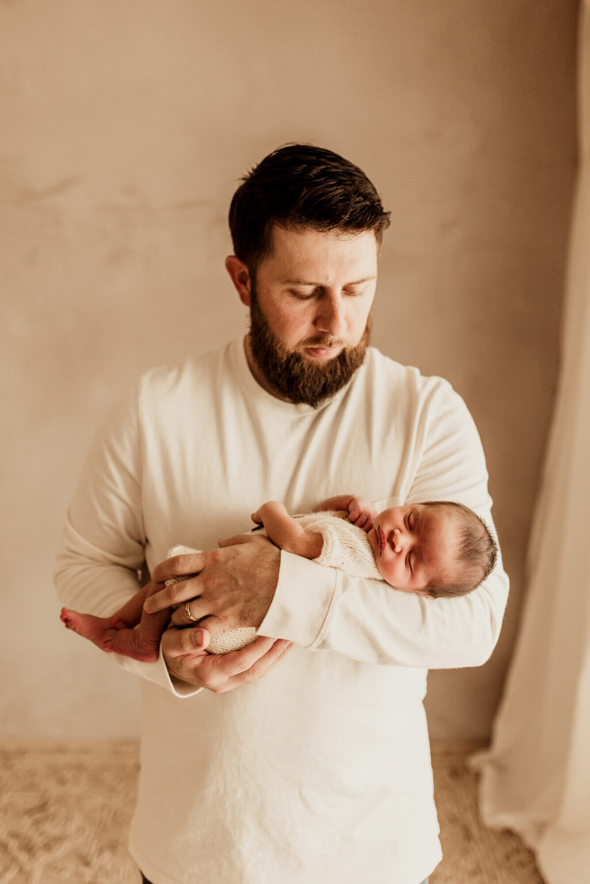 Father wearing a cream colored shirt cradles his  two week old son.