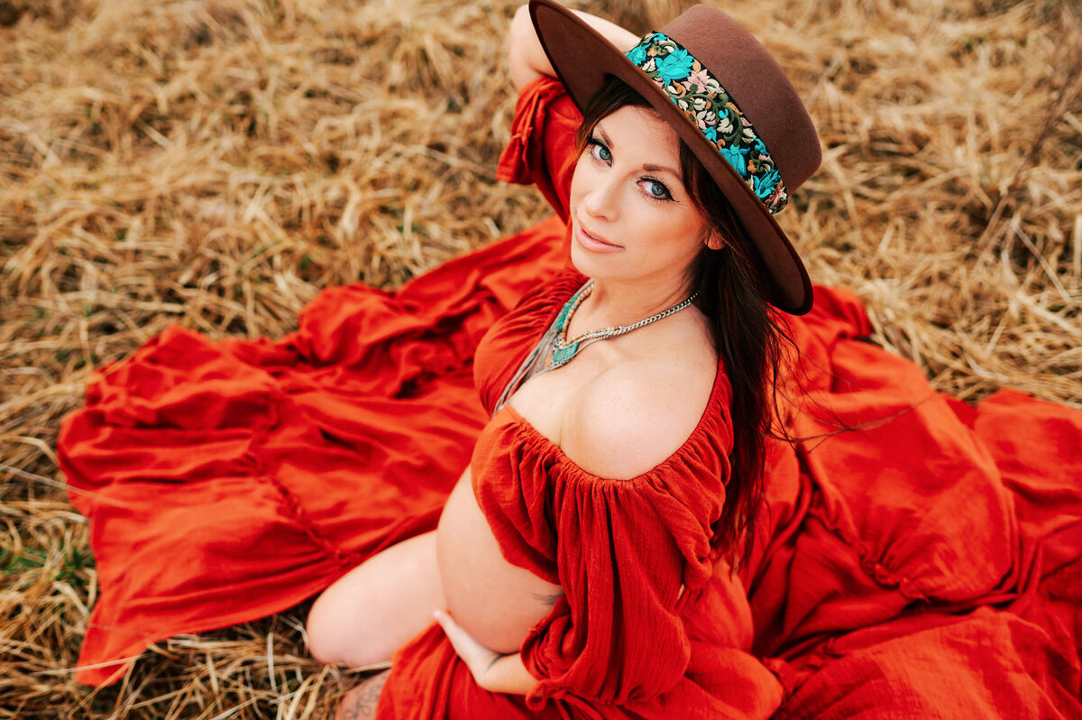 pregnant mom kneeling in field in red dress enjoying maternity photography in Joplin MO