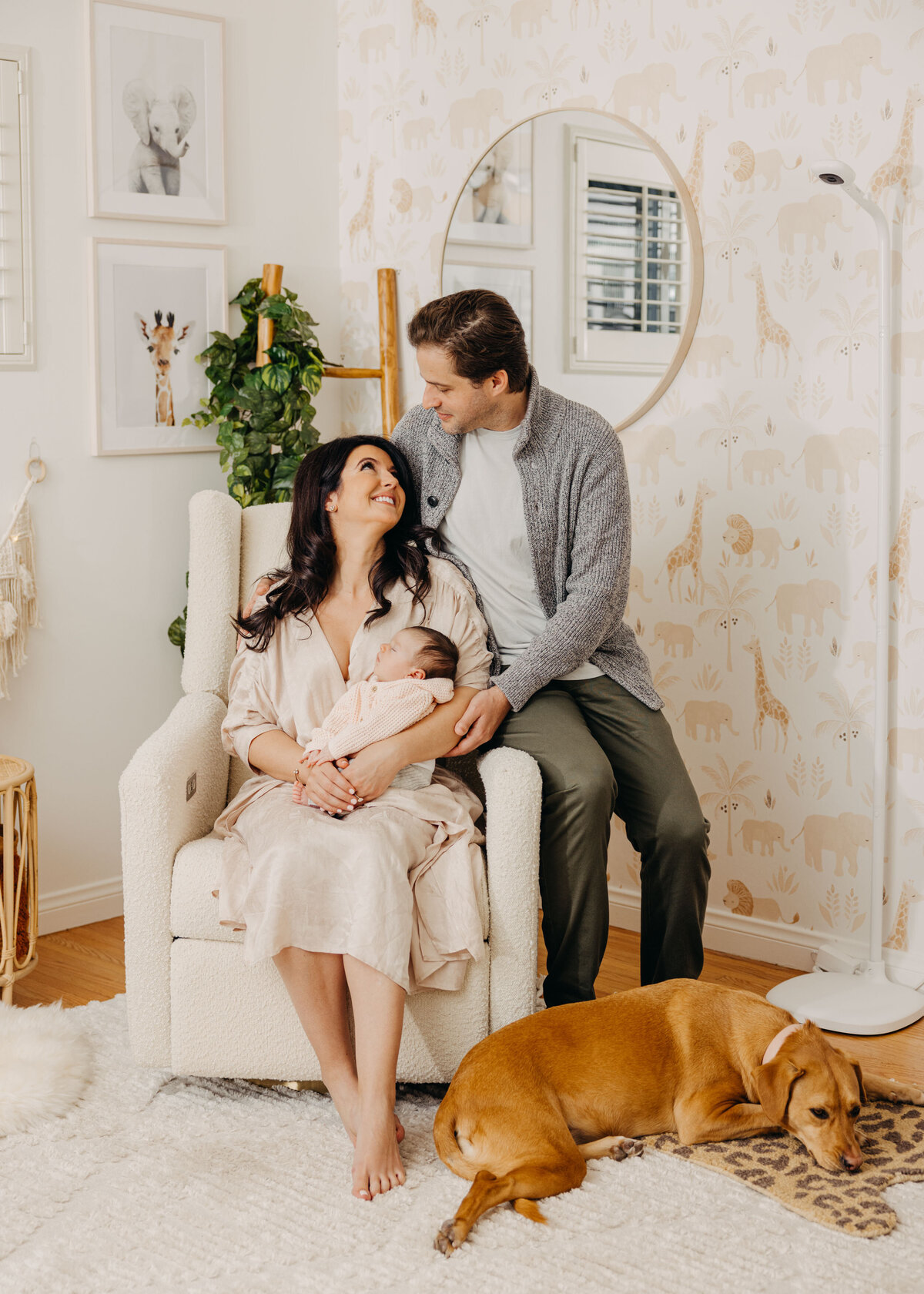 Family sitting in adorable jungle themed nursery with newborn baby and dog.