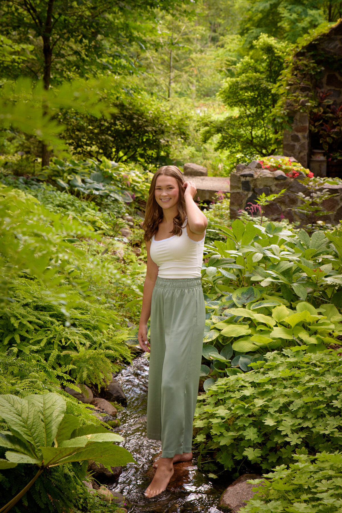 Luxemburg Casco High School senior girl wearing long sage green pants standing by creek in the hosta garden at the Green Bay Botanical Gardens in Green Bay, Wisconsin