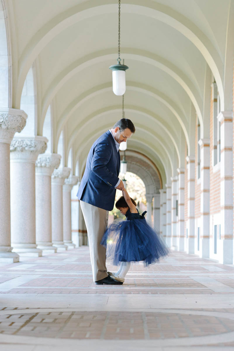 little girl in blue dress standing on dad's feet on Rice University Campus