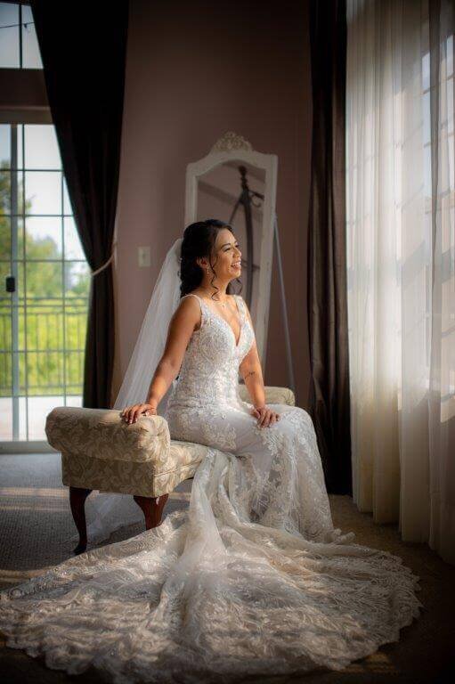 A bride sits in the getting ready area of Wolf Heights looking out a window and smiling. Photo by sacramento wedding photography studio philippe studio pro.