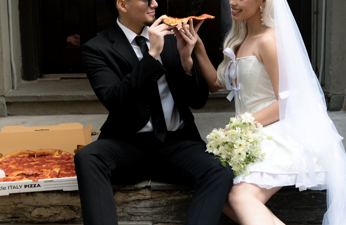 A creative shot of the pizza box open on a street corner in NYC, with the couple laughing in the distance.