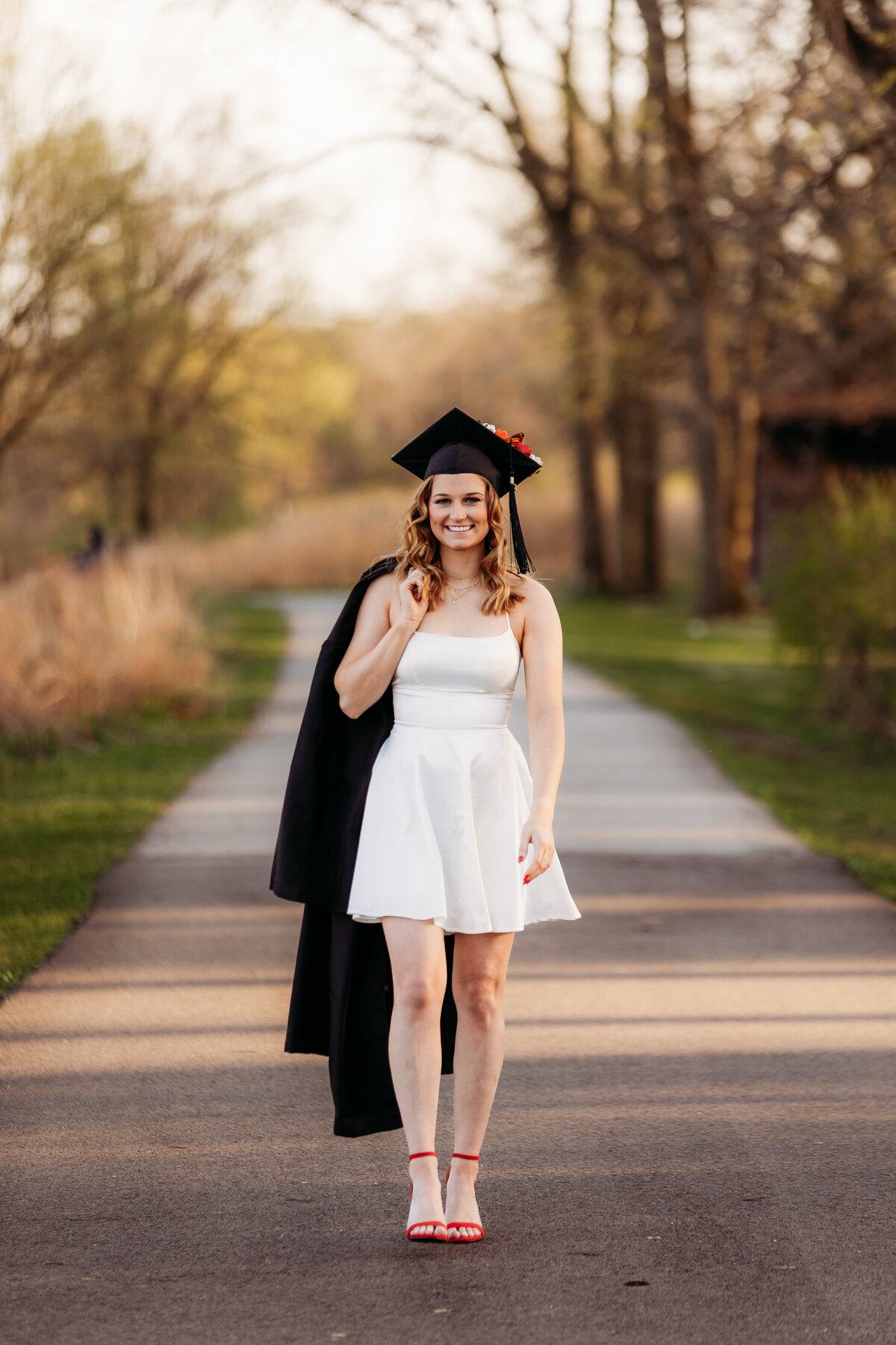A graduate walks down a path with her cap and gown.