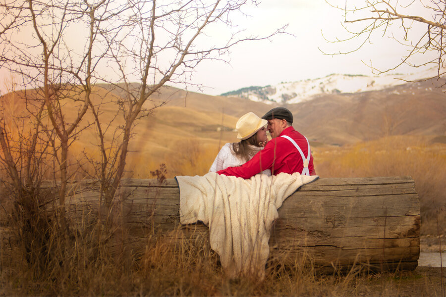 Couple sitting on wood log bench going in for a kiss in the fall.