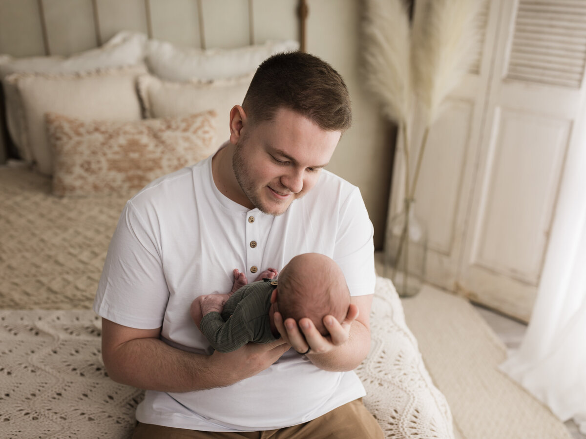 dad in white tshirt holding newborn baby boy in green onesie