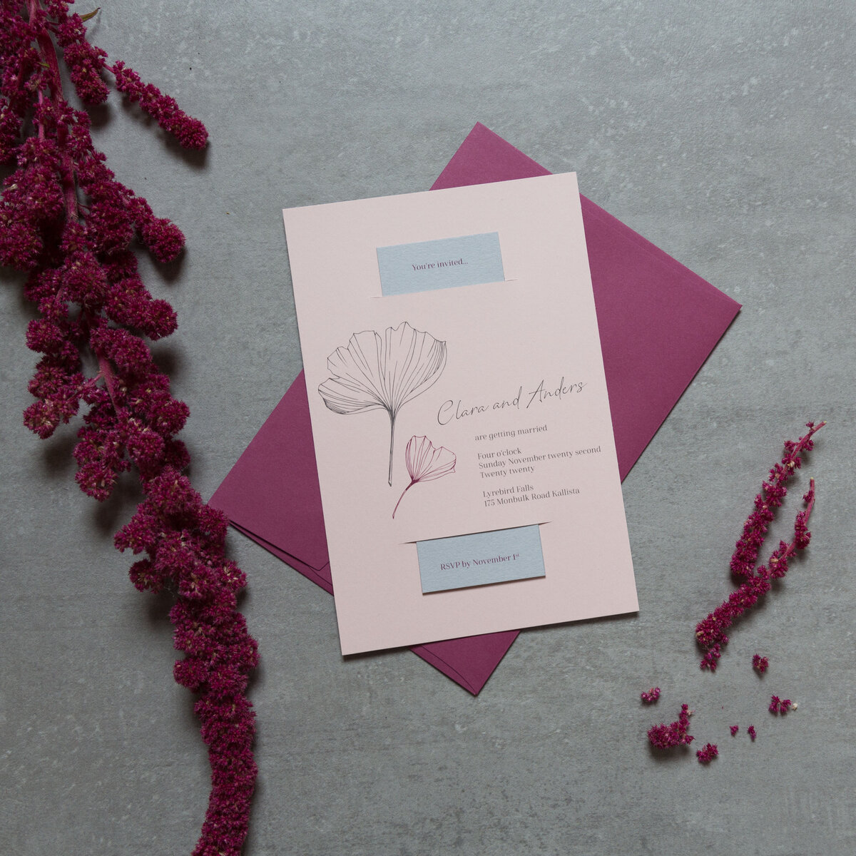 Pink and purple wedding invitation with a ginkgo leaf graphic and a grey RSVP card sitting inside the invitation.