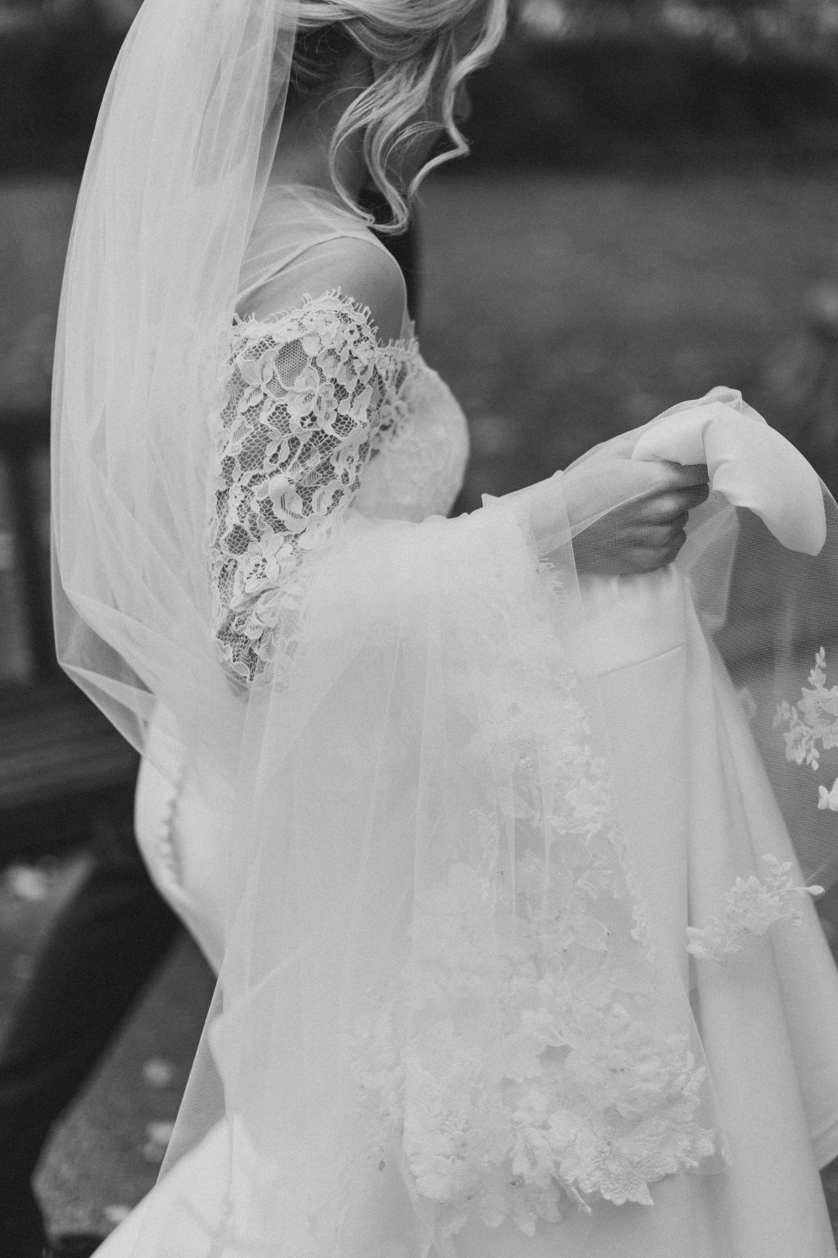 bride holding dress as she walks through park on wedding day