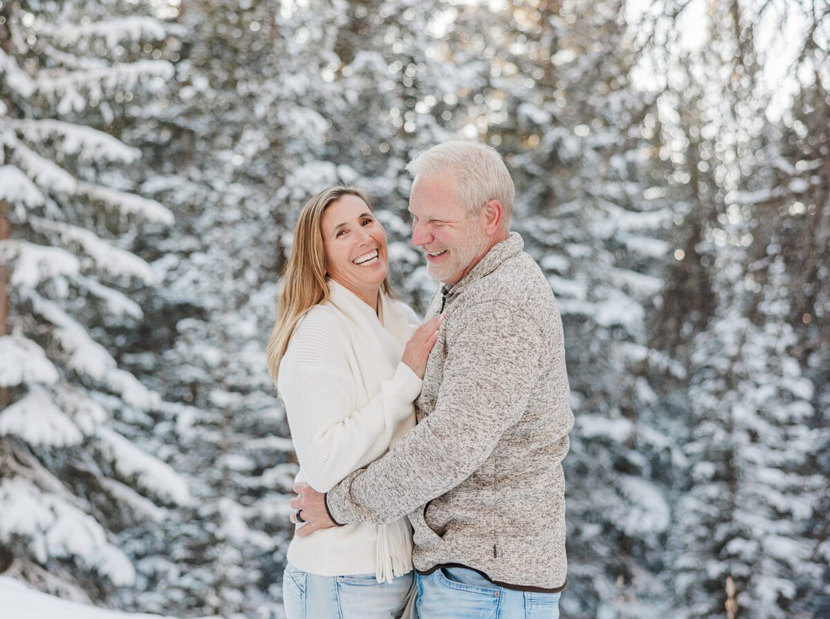 Laughing mom and dad hug in a snowy forest