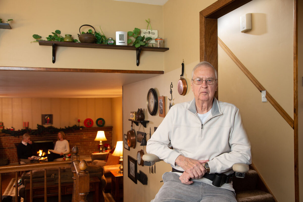 An elderly man is sitting in a mobility chair in a living room