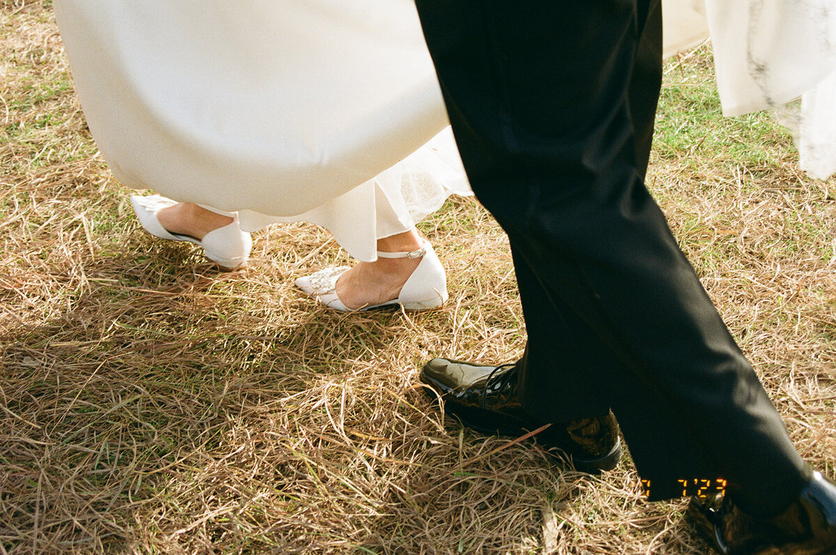 Bride and groom's shoes while walking through grass.