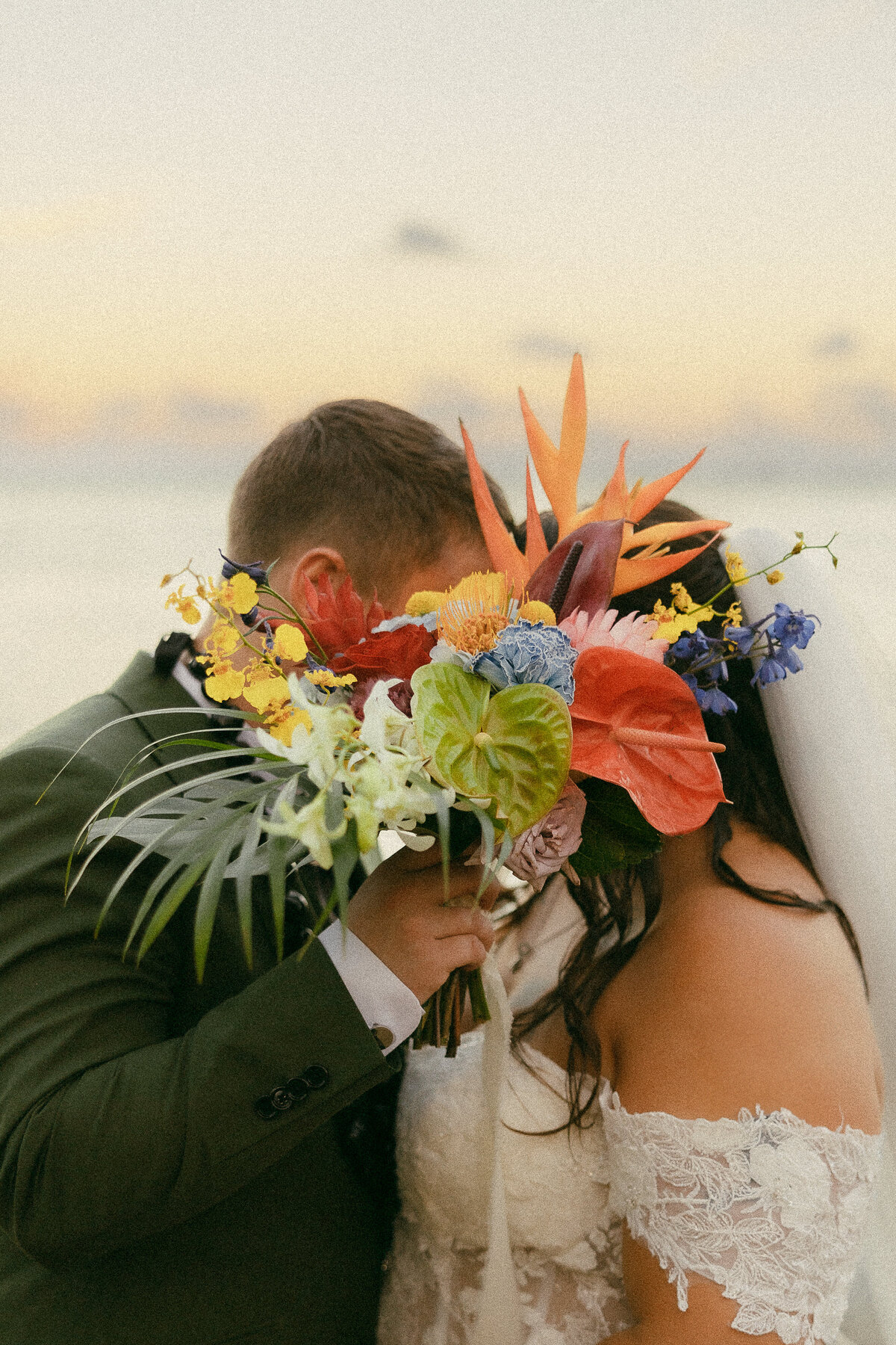 A person holding up a bouquet of flowers over their face as they kiss someone.