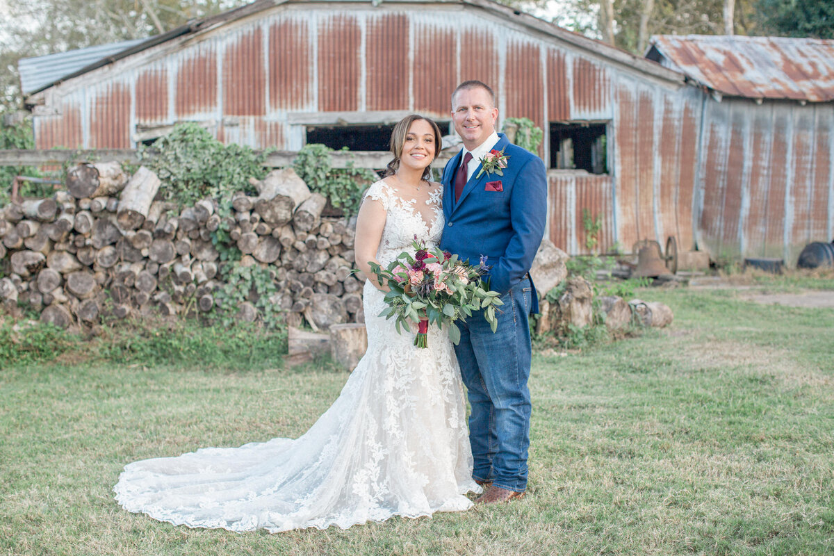 The bride & groom smile for their Colorado wedding photographer in front of a rustic barn